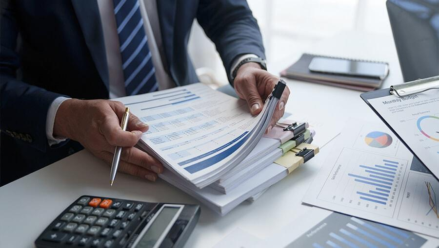 Finance professional reviewing stacks of paperwork, tax forms, and payment documents at a desk